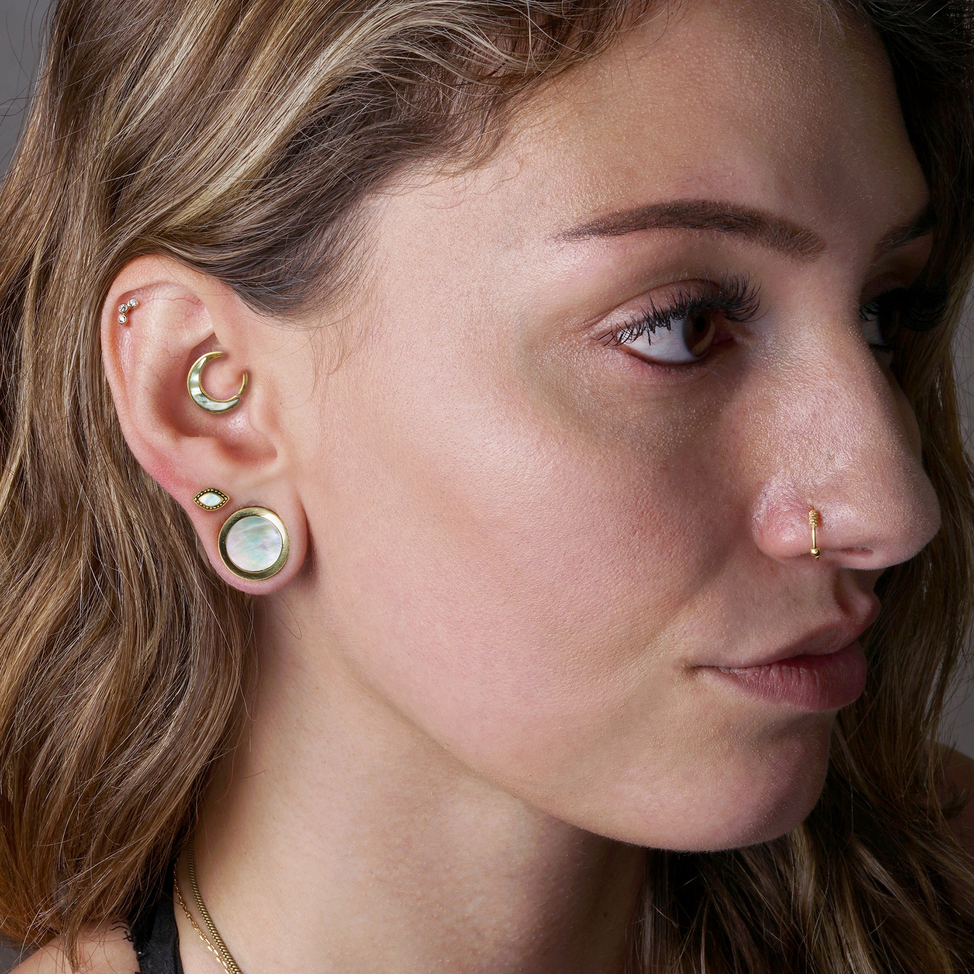 model wearing Golden Plugs with a Mother of Pearl, Aanya piercing ring on her daith and Golden Agatha Labret with MOP on her upper lobe