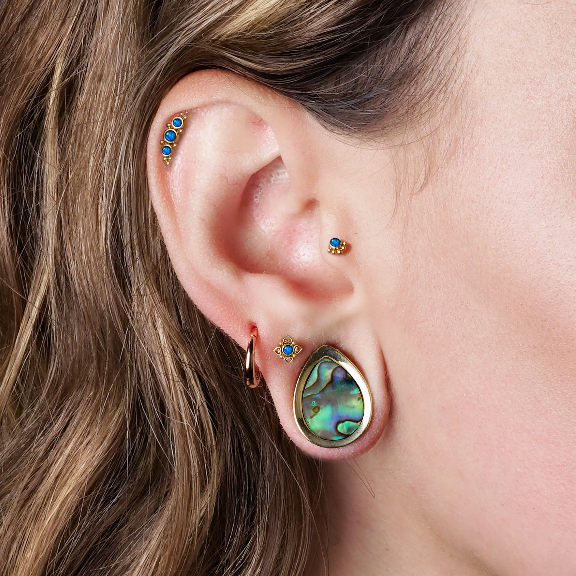model wearing Neptune Golden Labret with Opal on her upper lobe, Deva Golden Labret with Blue Opal on her helix and Layla Golden Labret with Blue Opal on her tragus