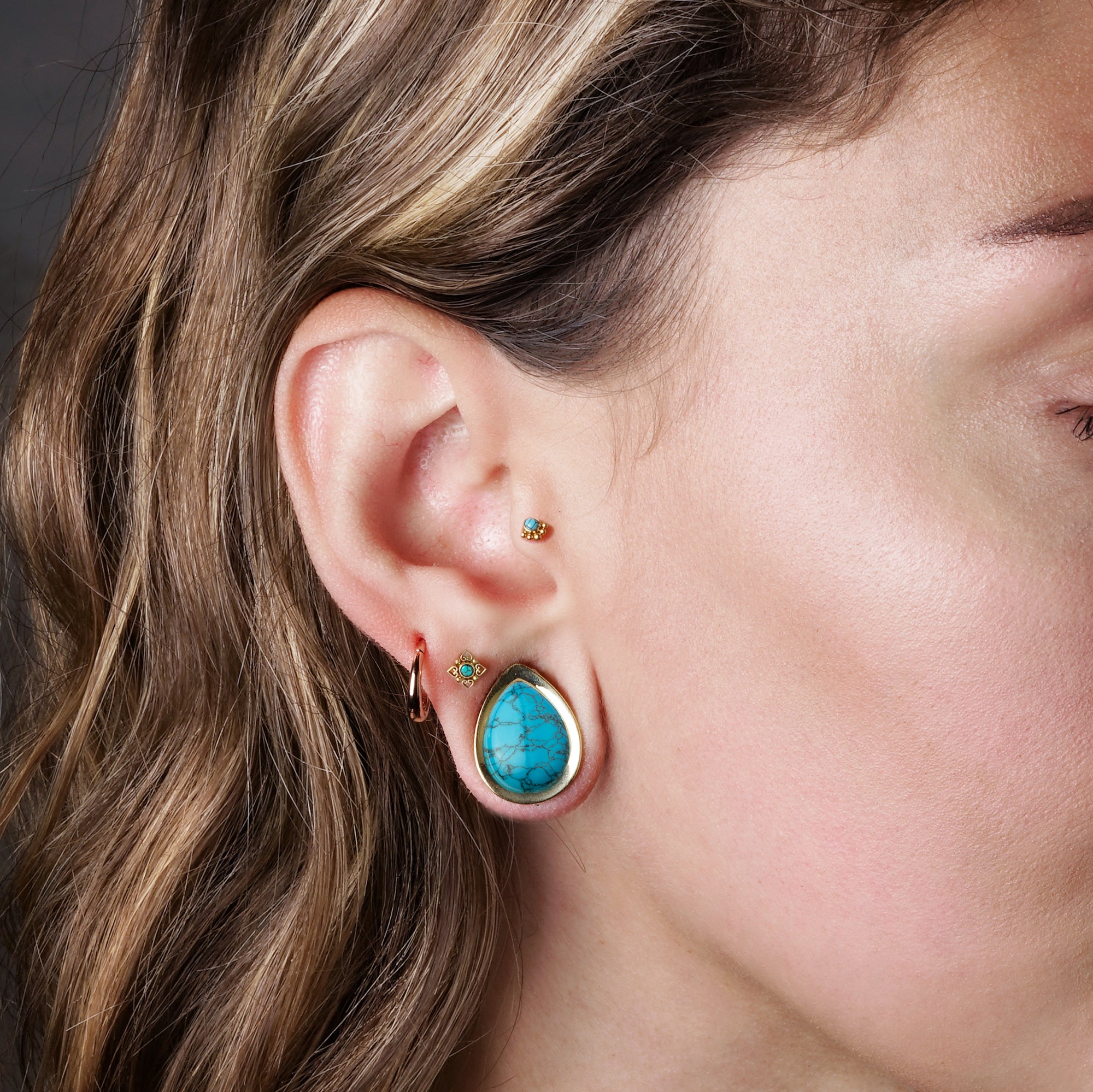 model wearing Teardrop Plugs with Turquoise, Layla Golden Labret with Turquoise on her tragus and Neptune Golden Labret with Turquoise on her upper lobe