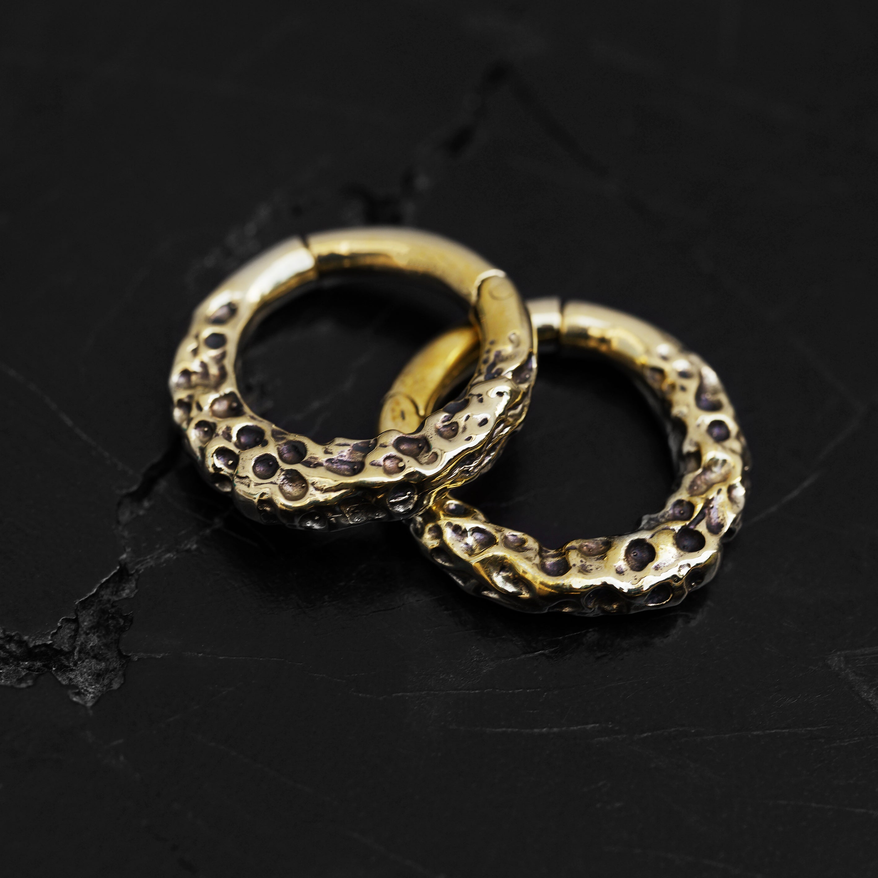 Pair of gold brass hoop hangers with rocky texture frontal view black background