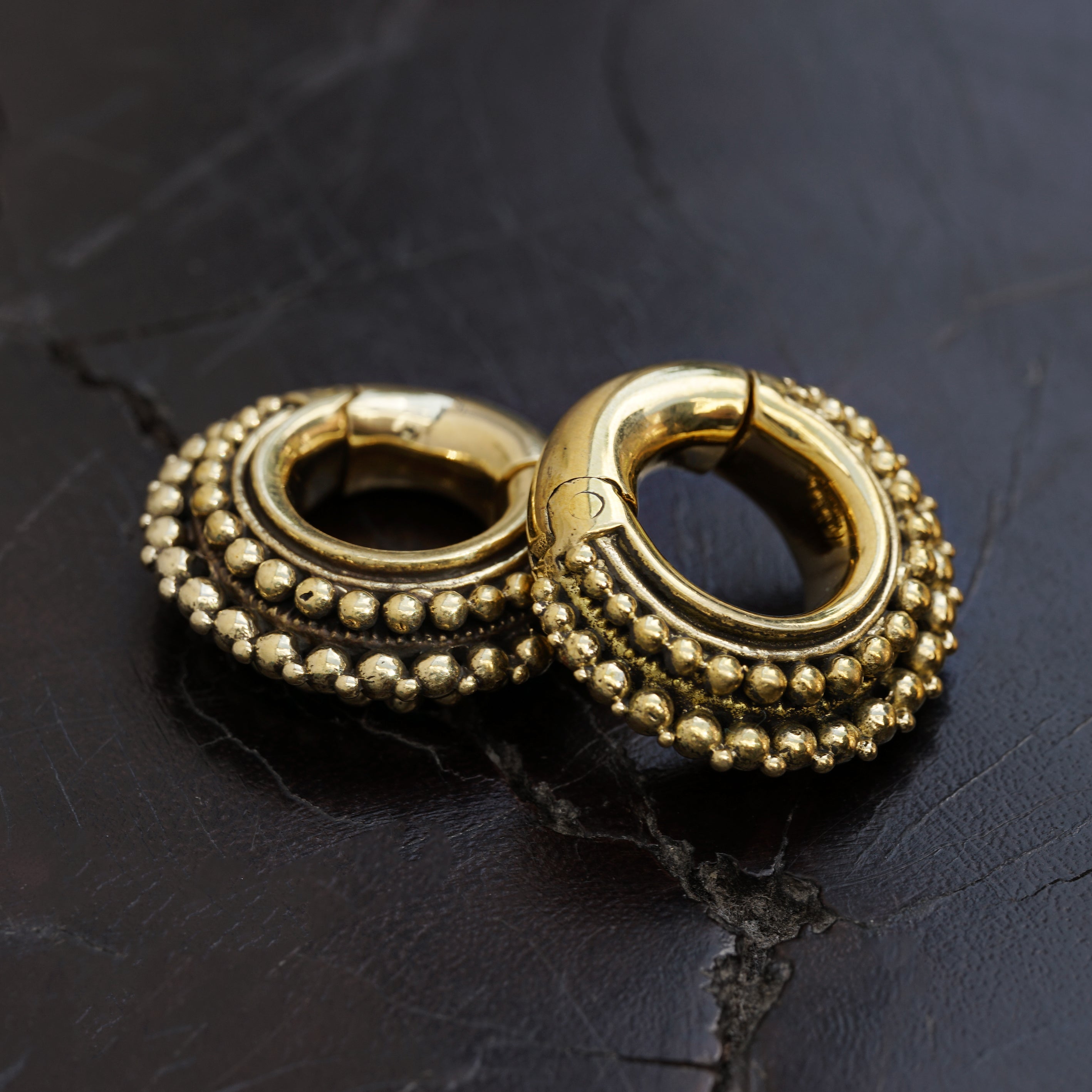 pair of gold brass chunky tribal ear weights hoops side black background view