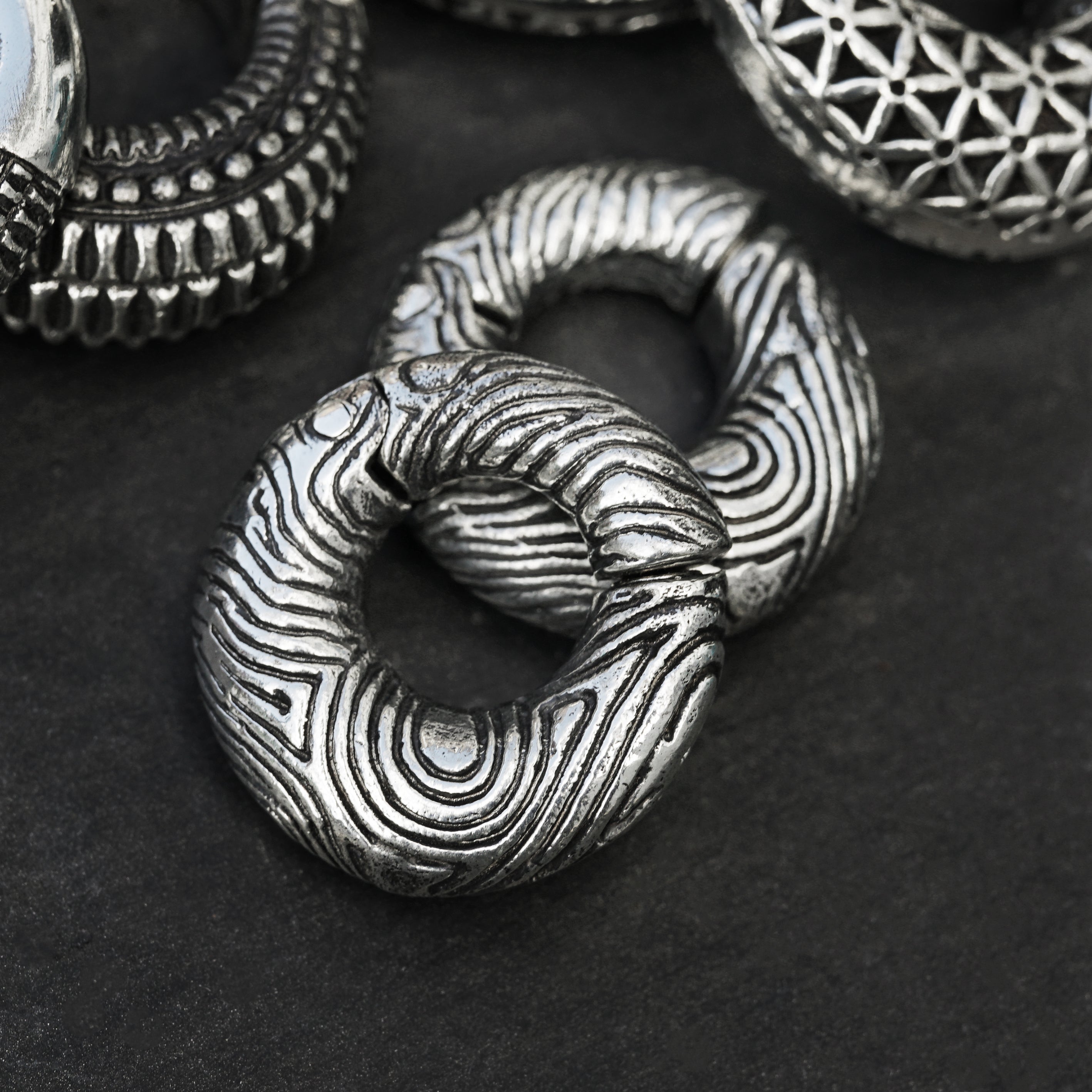 pair of silver brass ear weights hoops with etched curved lines frontal view black background