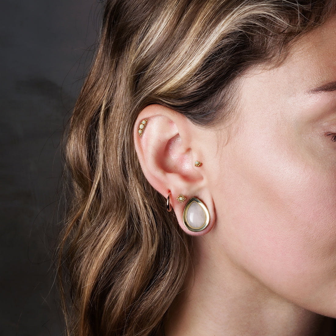 model wearing Neptune Golden Labret with White Opal on her upper lobe, Deva Golden Labret with Opal on her helix and Layla Golden Labret with Opal on her tragus