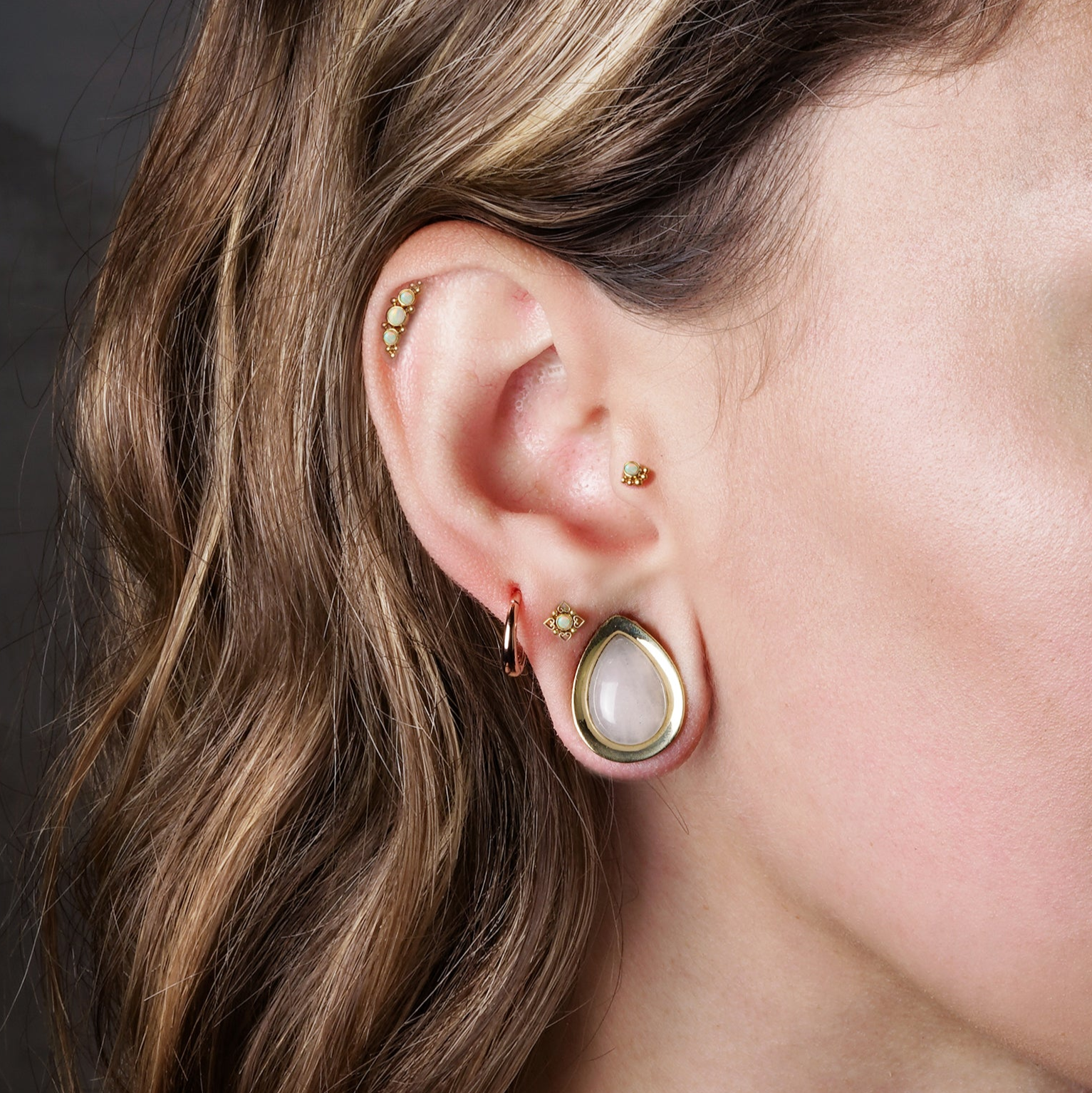 model wearing Neptune Golden Labret with White Opal on her upper lobe, Deva Golden Labret with Opal on her helix and Layla Golden Labret with Opal on her tragus