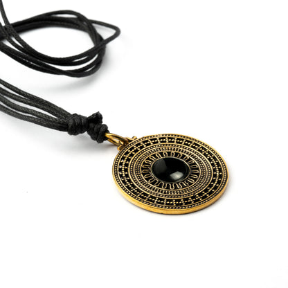 golden brass mandala pendant with centred black onyx stone on an adjustable cotton string close up view