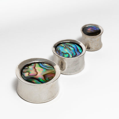 several sizes of silver ear plugs with abalone inlay close up view