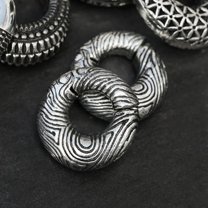 pair of silver brass ear weights hoops with etched curved lines frontal view black background